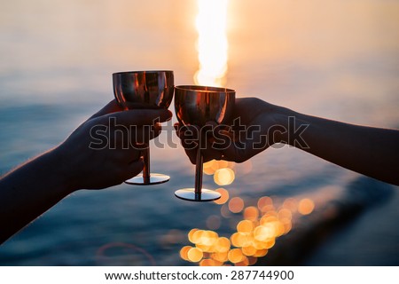 Celebrating love. Man and woman clanging iron glasses with champagne at sunset river background