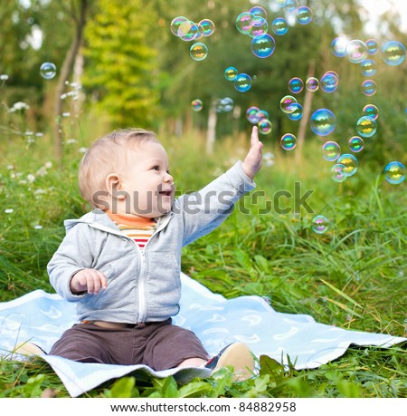 baby boy sitting on green grass outdoor playing with soap bubbles