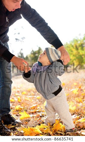 baby boy taking first steps with father help in autumn park