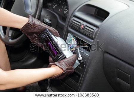 Gloved hands of a thief stealing a car radio from the dashboard of a car with the wiring exposed