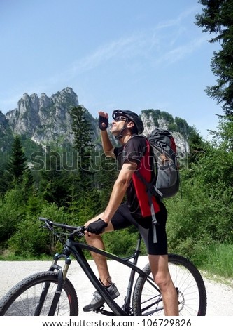 Athletic mountainbiker with a rucksack on his back pausing on his bicycle to look up at the mountain