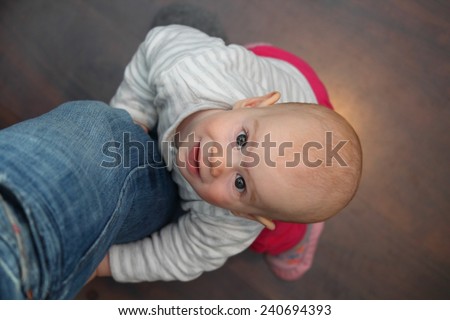 A 8 month old baby lifting up on the fathers leg