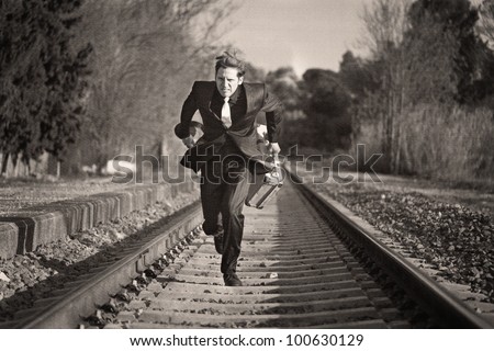 Young man running down the railway tracks with luggage and suit