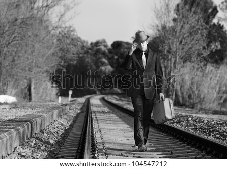 Man with suit , hat and suitcase walking across the railway