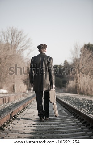 Young man backward with hat and old open suitcase in rail way