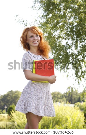 Portrait of Redhead woman, student stands in the park with books, during spring / summer time . Happy smiling beautiful young university student studying.