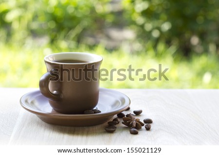 Brown Cup of coffe on wooden table in garden. Coffee Cup and saucer on napkin. Star anise and coffee beans
