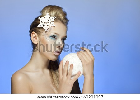 Snow-queen, Ice-queen. Young woman in creative image with silver blue artistic make-up and snowflake in hair and snow ball on blue background. New Year, Winter, Christmas image.Christmas decoration.