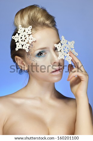 Snow-queen, Ice-queen. Young woman in creative image with silver blue artistic make-up and snowflake in her hair and arm on blue background. New Year, Winter, Christmas image. Makeup.
