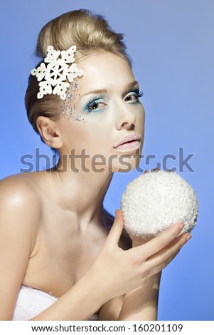 Snow-queen, Ice-queen. Young woman in creative image with silver blue artistic make-up and snowflake in hair and snow ball on blue background. New Year, Winter, Christmas image.Christmas decoration.