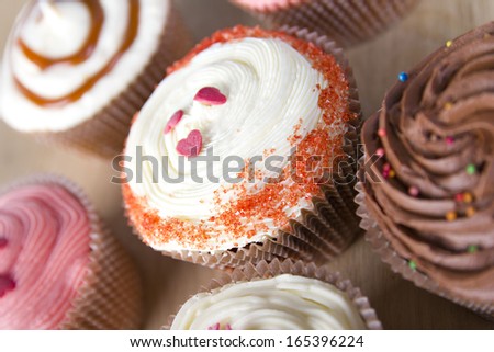 Close up set of colorful cupcakes on wooden background, brown table. Chocolate Cupcake, strawberry pink, bright white vanilla. Cafe, restaurant, sweets, cakes.
