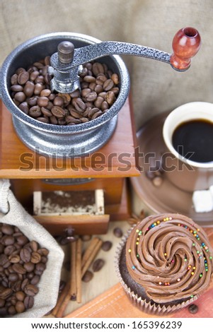 Retro coffee grinder, coffee mill coffee cup, chocolate ?upcake, coffee beans, cinnamon, star anise on sacking background. Still, restaurant, coffee shop.