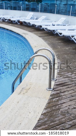 Hotel swimming pool. Grab bars ladder in the blue swimming pool. Sunbeds