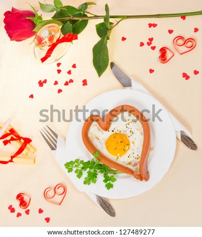 Festive a breakfast on Valentine\'s Day, sausage in the form of heart, fried egg, red rose, notes with prediction, bottle of perfume with red ribbon on tablecloth