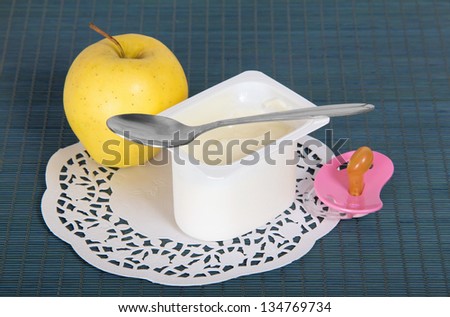 Box with yogurt, apple,soother and a napkin on blue background