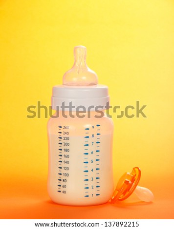 Bottle with milk and a soother on an orange background