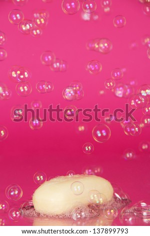 Piece of toilet soap and soapsuds with air bubbles texture, on a pink background