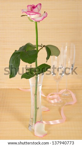 Rose in a vase, wine glasses and a ribbon on a bamboo cloth