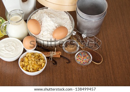 Milk, sour cream, flour, raisin and spices for an Easter cake, on a brown background