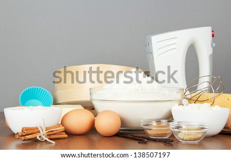 Flour, dairy products, eggs, spices and mixer on a table, on a gray background