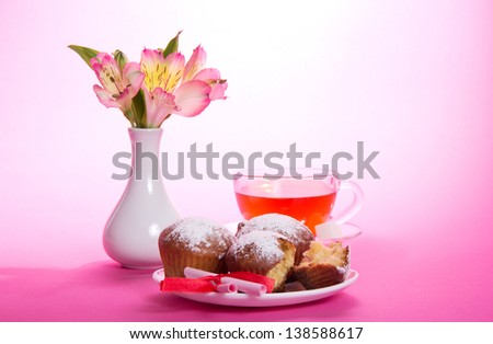 Cakes on a dish and a cup of tea, a note with a ribbon, flowers in a vase, on a pink background