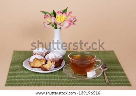 Tea, cupcakes and vase with the flowers on a bamboo cloth, on a beige background