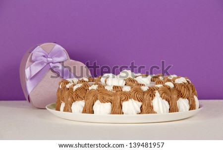 Dish with a biscuit, a gift a heart on a white cloth, on a violet background