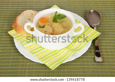 Bowl with soup, bread, a plate, a spoon and a napkin on a green bamboo cloth