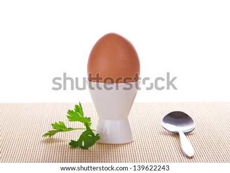 Boiled egg in a support and a spoon on the bamboo cloth, isolated on white