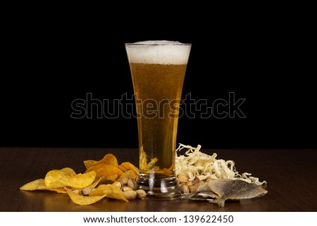 Glass of foamy beer with bubbles, chips, salty fish, dried squid and the pistachios on the table
