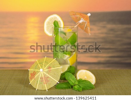 Mojito with umbrellas, a lemon on a green bamboo cloth against the sunset