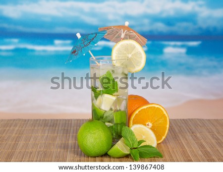 Mojito with umbrellas, orange, a juicy lime, a lemon on a bamboo cloth against the sea