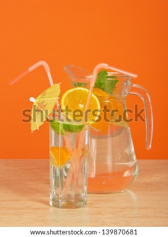 The drink glass with a straw, is decorated with an umbrella and an orange segment, a jug on a table