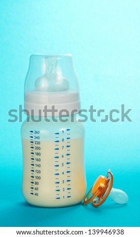 Bottle with milk and a soother on a blue background