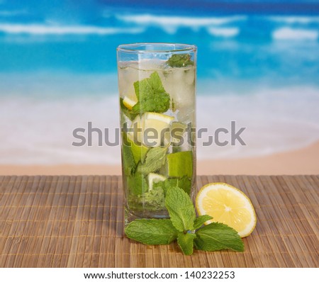 Glass with a mojito, a juicy lime and a spearmint leaf, on a bamboo cloth against the sea