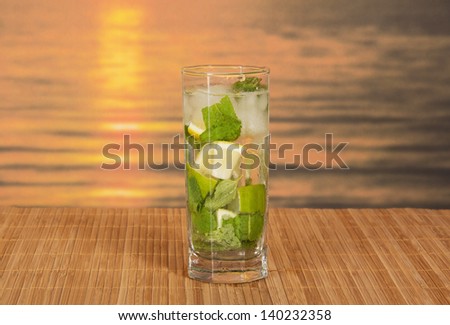 Green alcoholic cocktail from a citrus and mint, on a bamboo cloth against the sunset