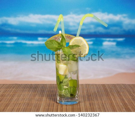 Mojito with cocktail straws and a lemon slice, on a bamboo cloth against the sea