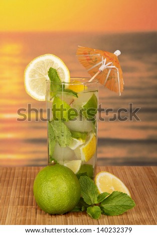 Glass with a mojito, a juicy lime and a spearmint leaf, on a bamboo cloth against the sunset