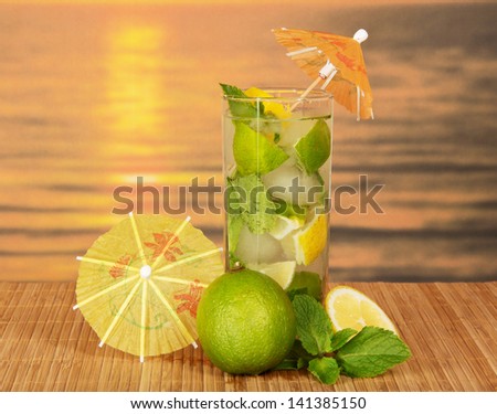 Mojito with umbrellas, a juicy lime, a lemon on a bamboo cloth against the sunset