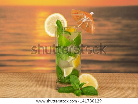 Cold drink with a lemon slice, spearmint, on a bamboo cloth against the sunset