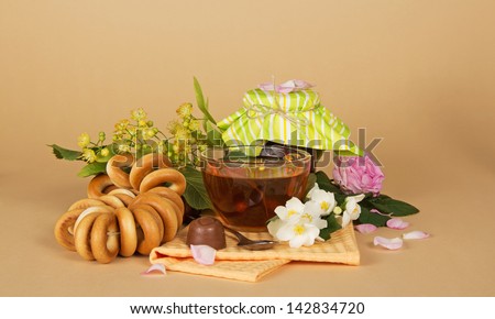 Cup of tea, heap of bagels, chocolate, and flowers on a beige background