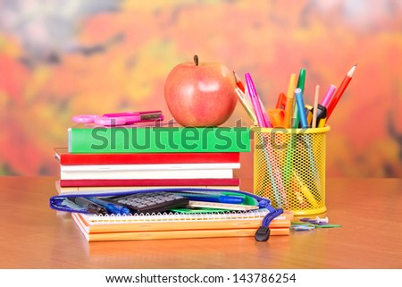Books, pencils and handles in a support, a pencil-case, a scissors and apple, on a table
