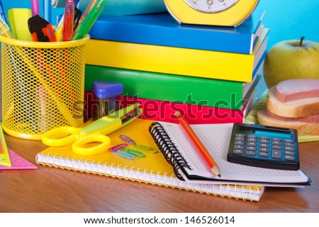 Pile of books, an exercise book office supply the calculator an alarm clock, apple and sandwich, closeup on a table
