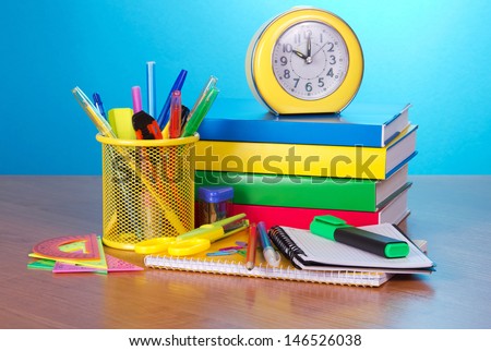 Pile of books, an exercise book, office supply, the calculator, and an alarm clock on a table