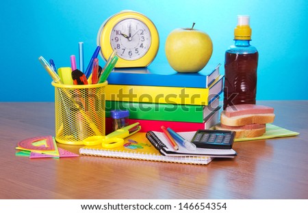 Books, an exercise book office supply alarm clock the calculator, apple, sandwich and a drink, on a table