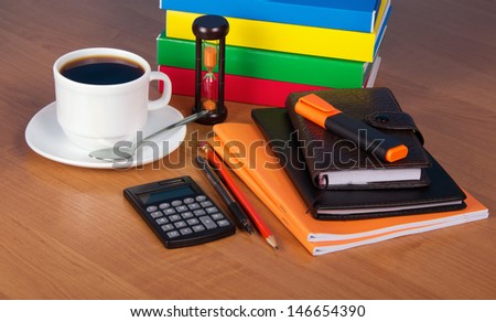 Notepad, exercise book, organizer, marker, books, the calculator, hourglasses and a cup of coffee on a table