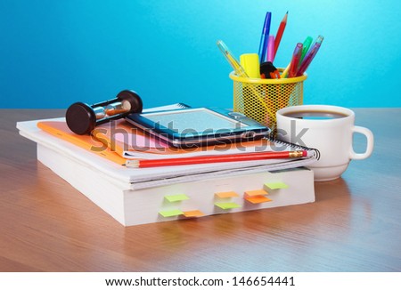 The book, hourglass, e-book, pencils and handles in a support, a cup of coffee on a table