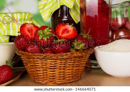 Jars of jam, a drink in a jug, basket with strawberry, glass with berries and cup with sugar, closeup, on a table