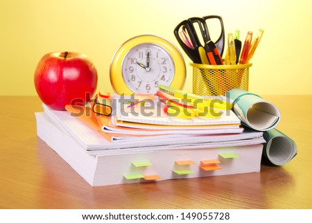 The book, a roll of exercise books, a support with handles, an alarm clock and red apple on a yellow background