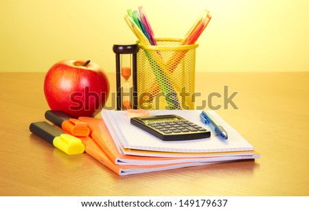 Exercise books, markers  a support with handles a hourglass and apple on a yellow background